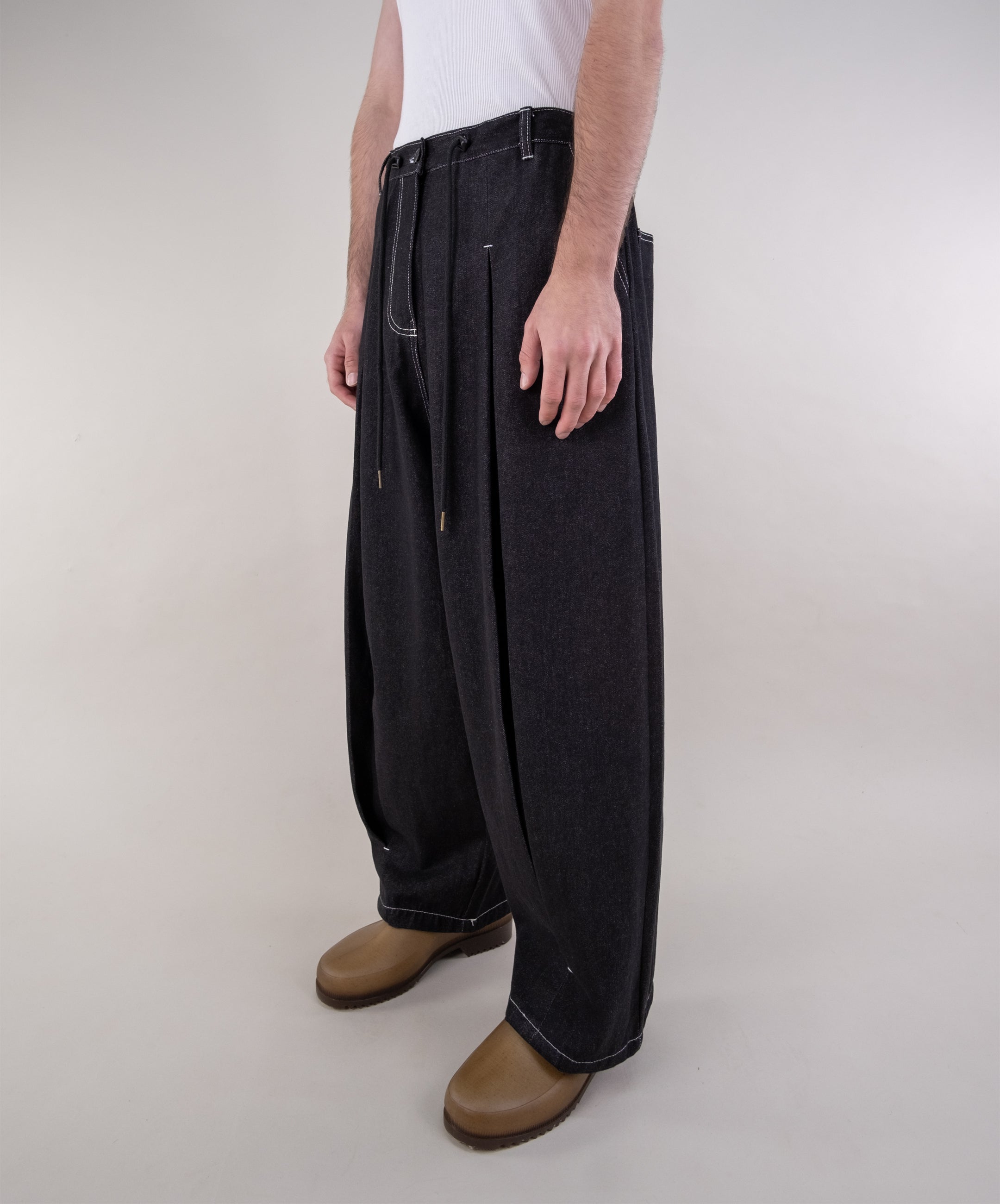 Person wearing black wide-leg jeans and brown shoes on a plain background